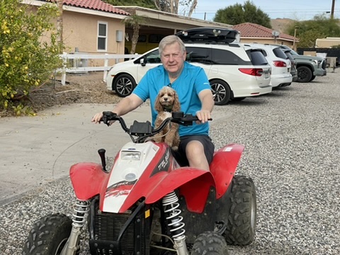 Ed riding a red four-wheeler with a small dog